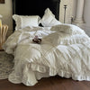 A white ruffled duvet cover set is displayed on a bed, featuring layered fabric and decorative ruffles.