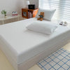 A white fitted bed sheet cover is displayed on a bed, next to a lamp and some books.
