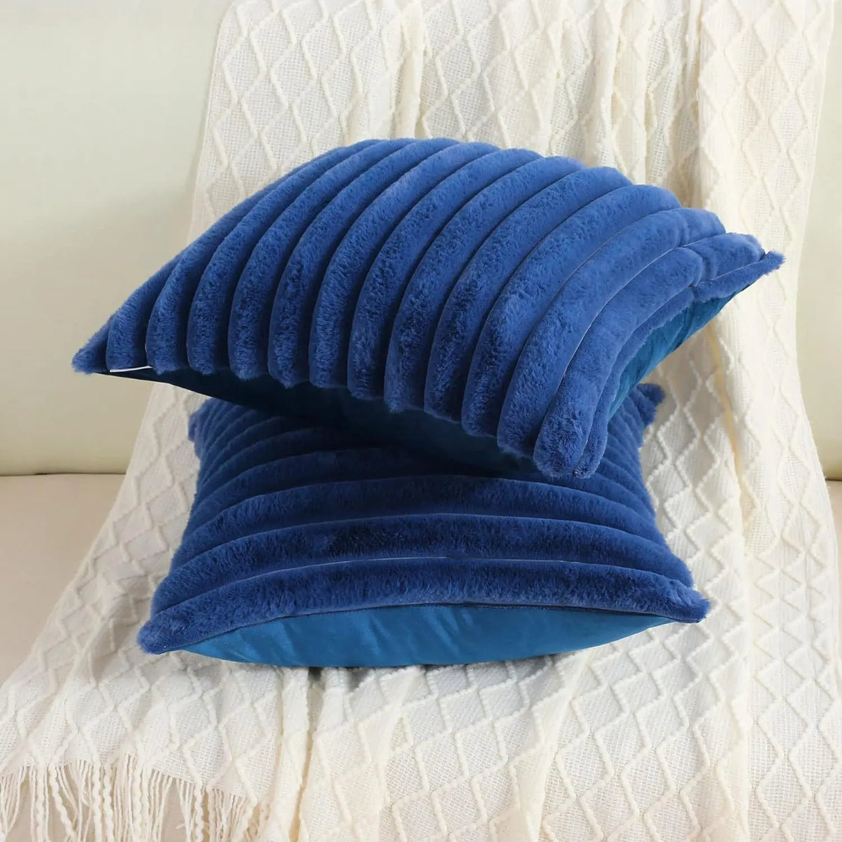 A stack of deep blue faux rabbit fur cushion covers resting on a white textured fabric.
