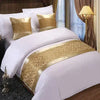 White bedding with gold patterned decorative bed flags on pillows and a golden lamp.