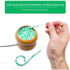 A hand is using a clip-style beading needle to thread a green bead spinner with a thin wire.