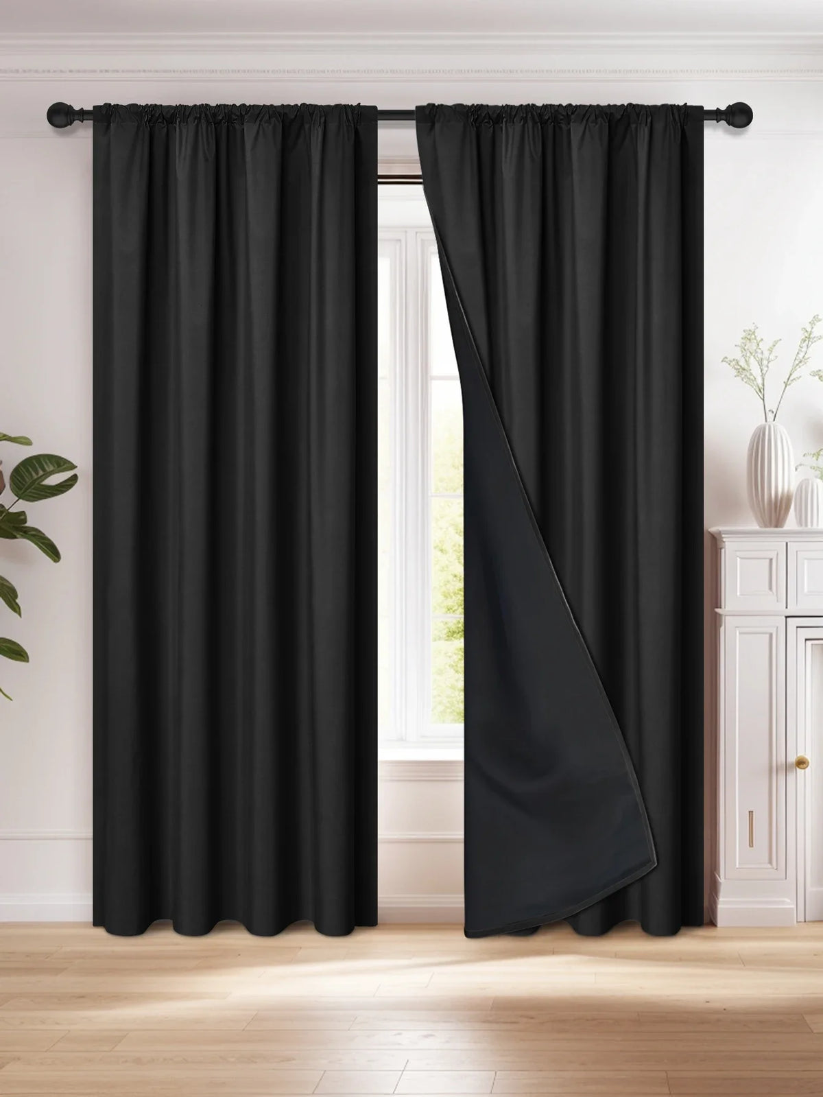 A floor-length black blackout curtain hanging from a rod, shown in a bright room.