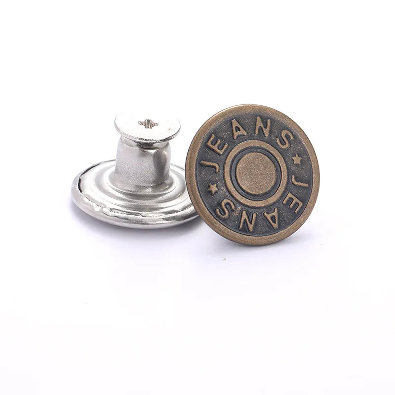 A round, antique brass metal button with the word JEANS stamped around the edge and a silver post.