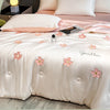 A light pink embroidered quilt with floral patterns and soft pink bedding is displayed on a bed.