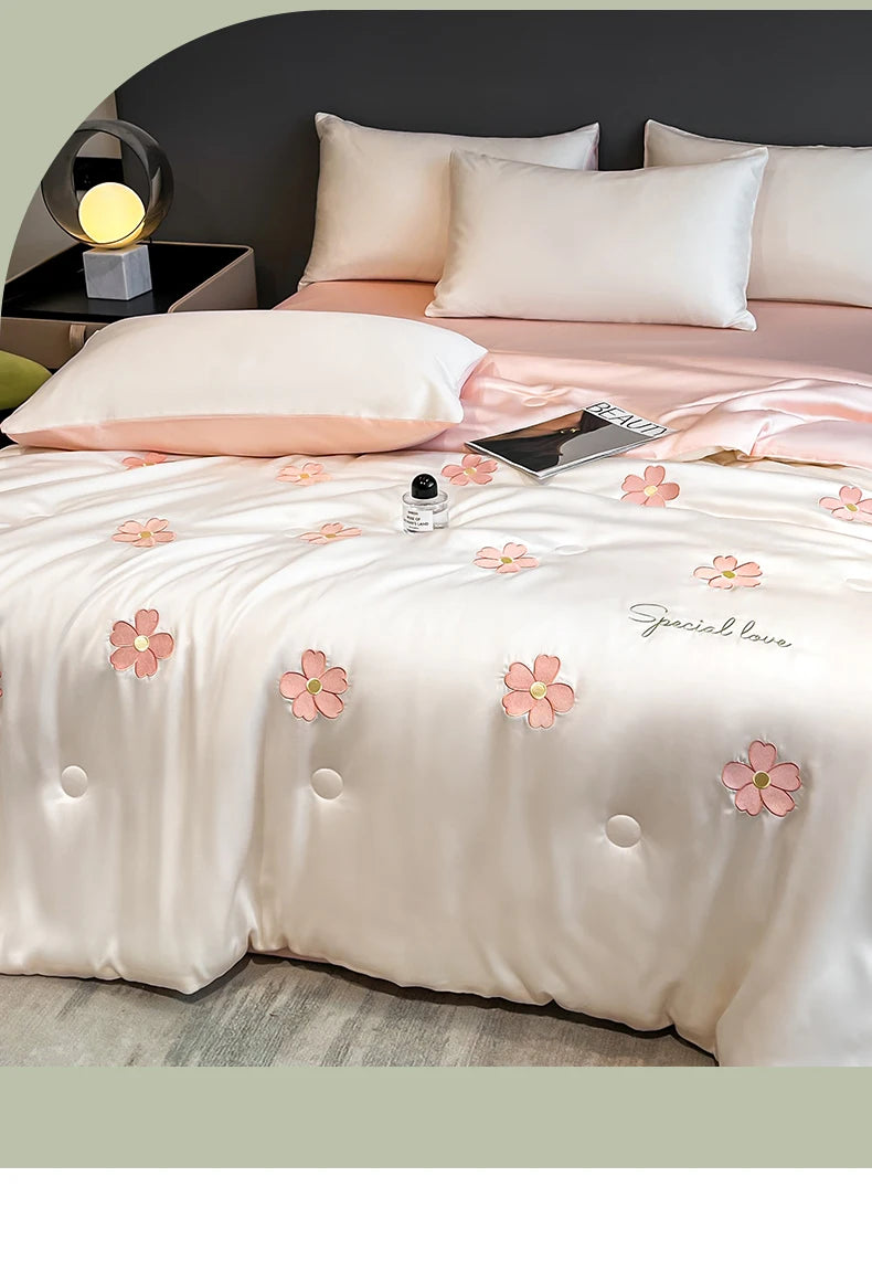 A light pink embroidered quilt with floral patterns and soft pink bedding is displayed on a bed.