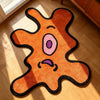 An orange and black playful one-eye monster area rug lying on a light wooden floor.