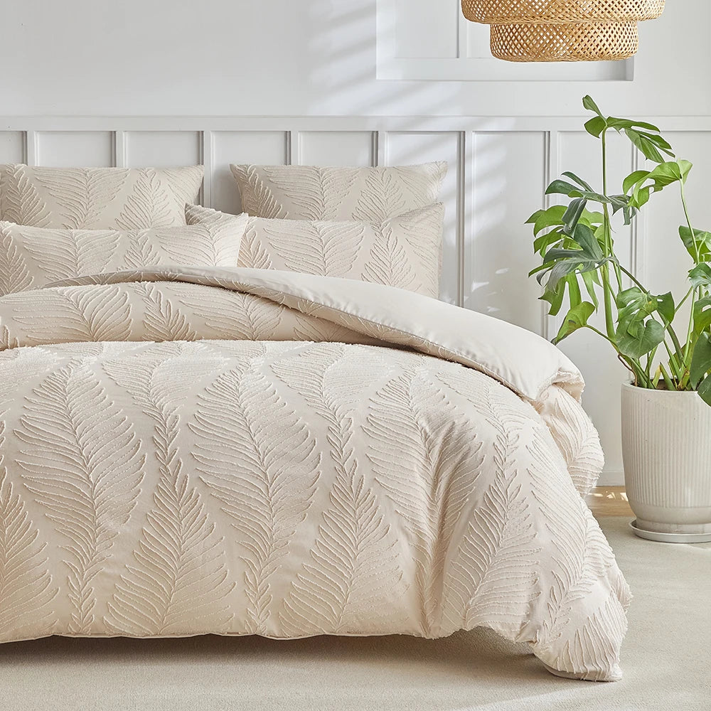 A beige luxury quilt duvet set with textured embroidery is displayed on a bed against a white paneled wall.