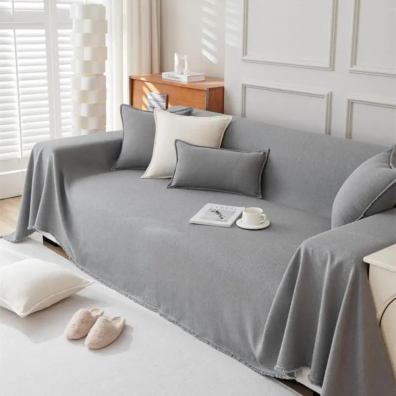 A light gray anti-scratch sofa cover draped over a modern sofa with decorative pillows and a small cup on the fabric.