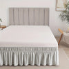 A white bed with a light gray upholstered headboard and a ruffled fabric skirt at the bottom.