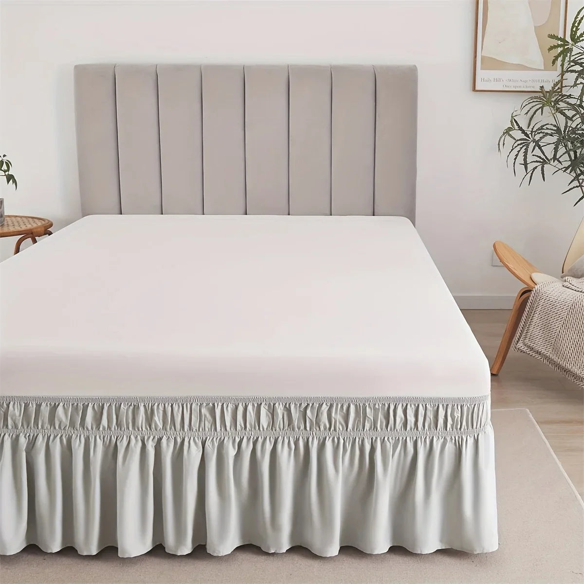 A white bed with a light gray upholstered headboard and a ruffled fabric skirt at the bottom.