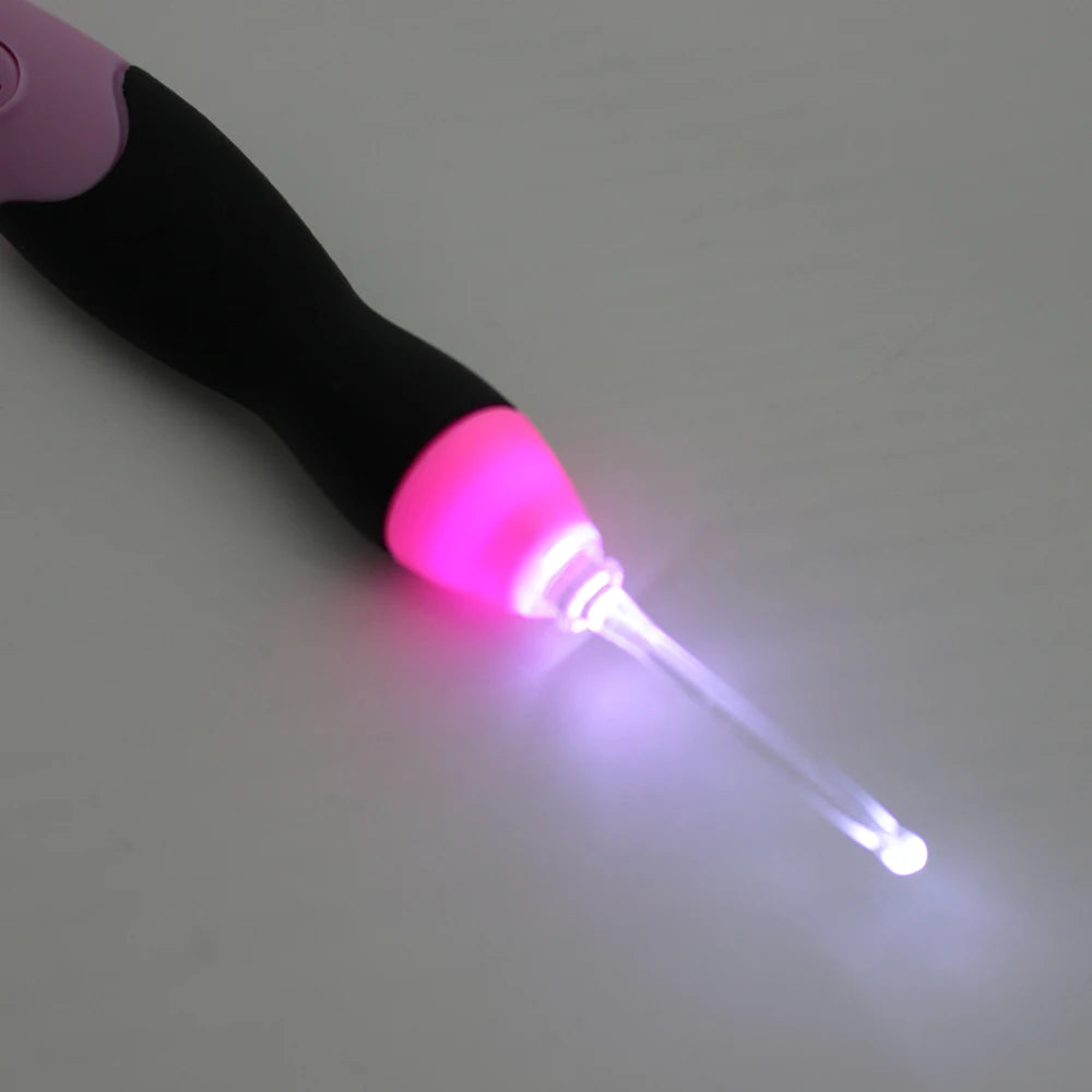 A close-up of a black and pink rechargeable LED crochet hook set with a glowing tip.