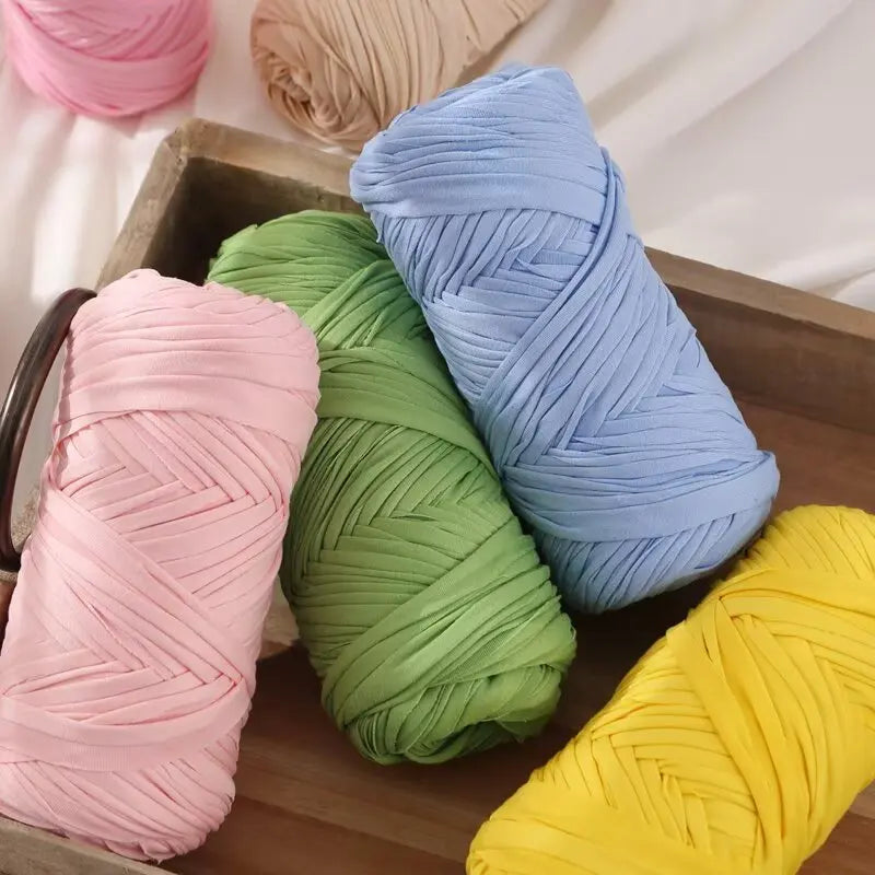 A collection of colorful reusable elastic yarn spools in pink, green, blue, and yellow resting in a wooden box.