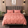A pink quilted bedding set featuring a duvet and pillows displayed on a bed with a gray upholstered headboard.