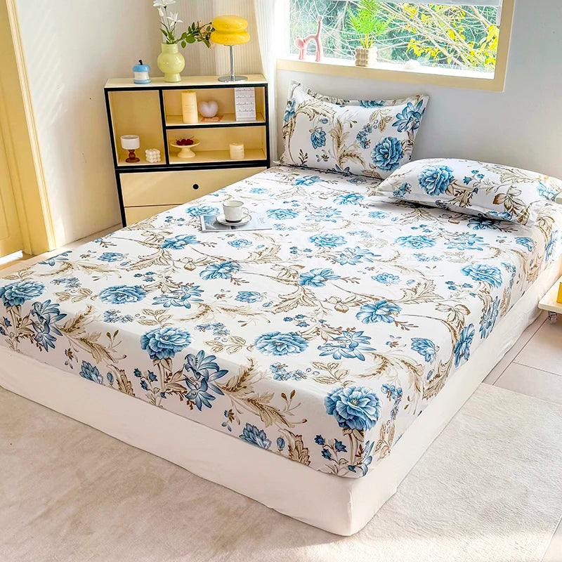 A fitted bed sheet with a blue and beige floral print is displayed on a white bed in a bright room.