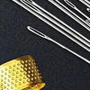 A close-up of precision stainless steel sewing needles and a gold-colored metal object on a dark background.
