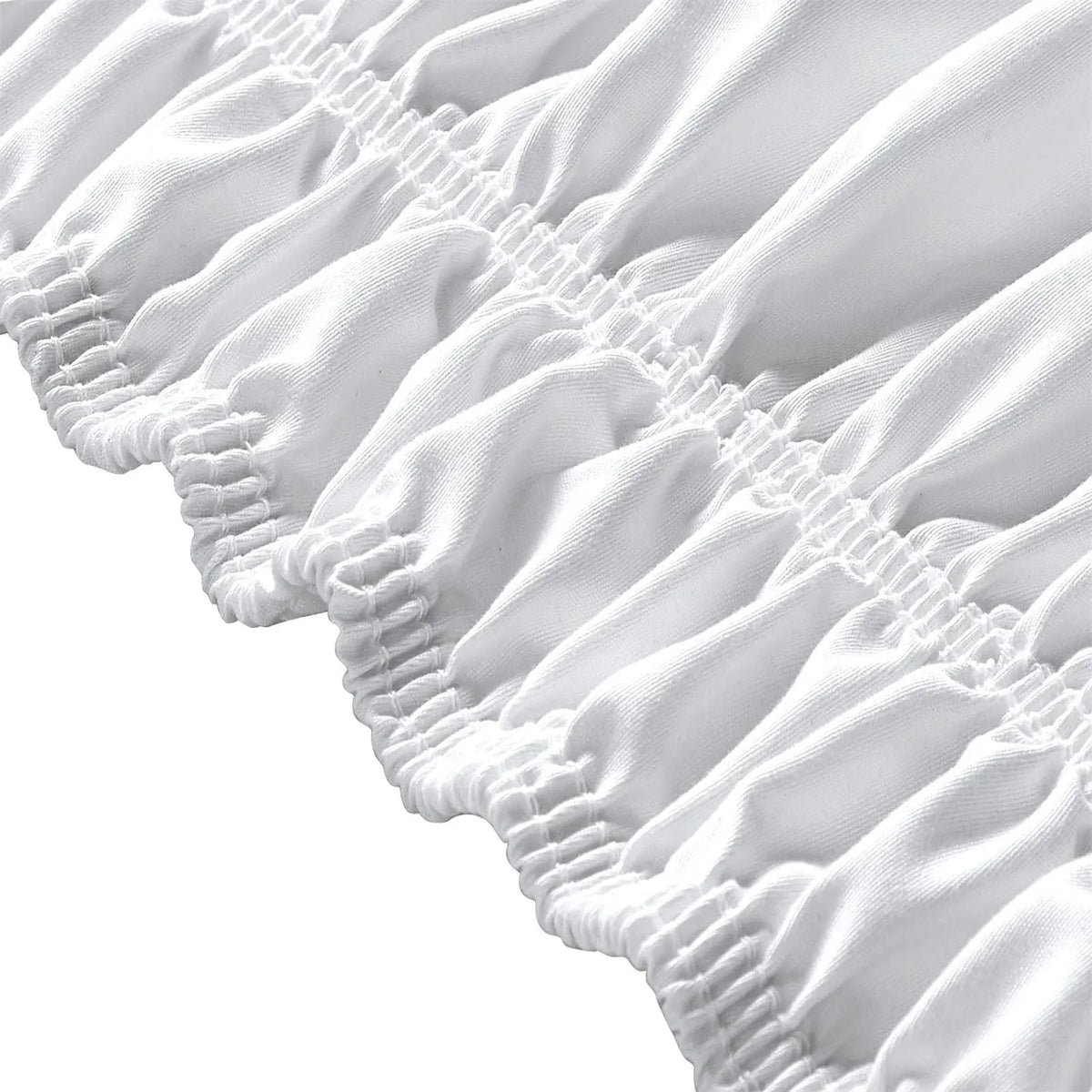Close-up of an elegant white elastic bed skirt featuring delicate ruffles and gathered fabric.