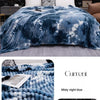 A blue tie-dye flannel fleece throw blanket draped over a bed, featuring white and dark blue patterns.