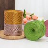 Spools of metallic cake yarn in gold and rose tones resting on a wooden surface.