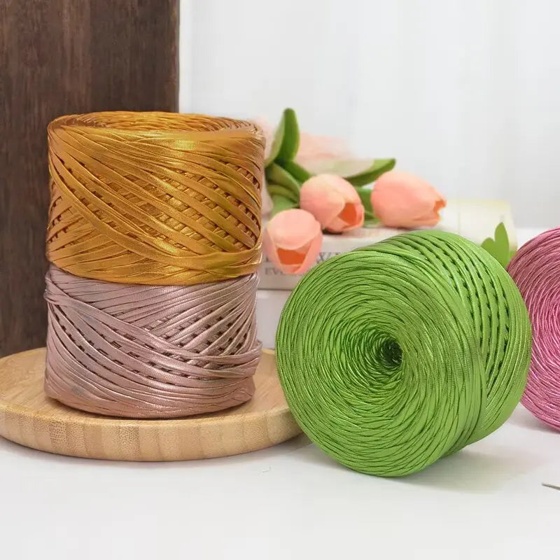 Spools of metallic cake yarn in gold and rose tones resting on a wooden surface.