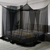 A floor-to-ceiling black mosquito net curtain draped over a bed in a room.