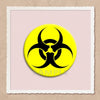 A yellow circular pin featuring a black biohazard symbol on a light pink background.