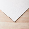 A white, rectangular wool blanket is placed on a light wooden surface.