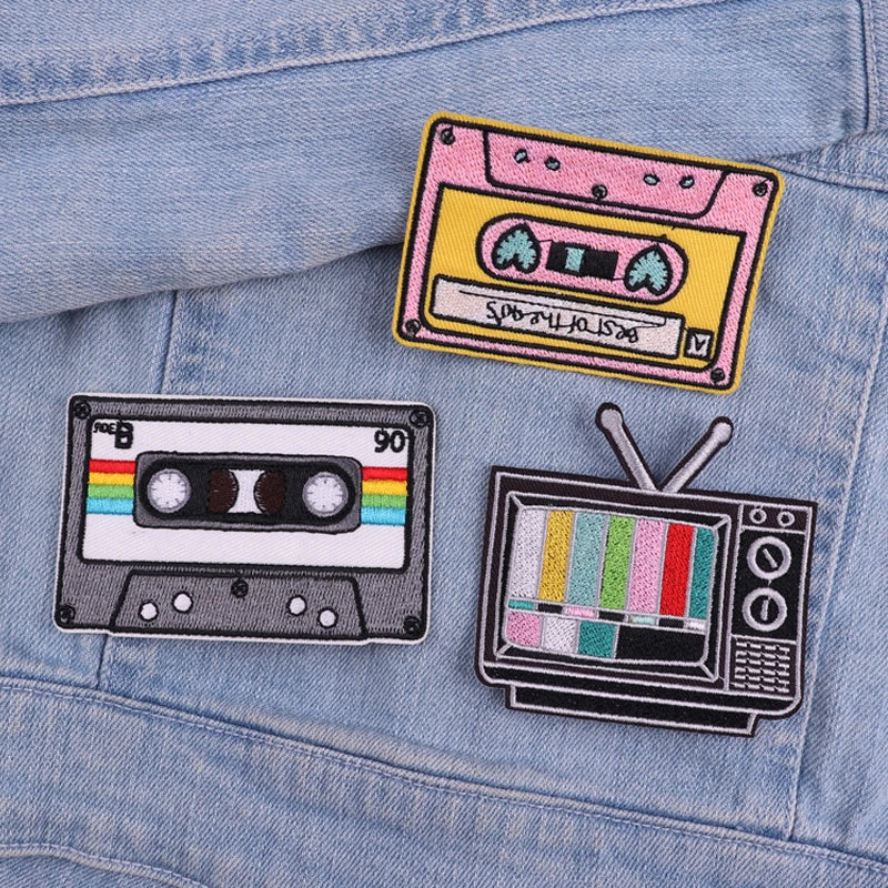 Three embroidered letter patches featuring a cassette tape, a yellow radio, and a television set on a light blue denim jacket