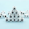 A collection of white alphabet beads A through K arranged in a pyramid shape on a light blue surface.