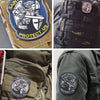 Close-up of St. Michael embroidered hook and loop tactical patches on camouflage fabric and a green jacket.