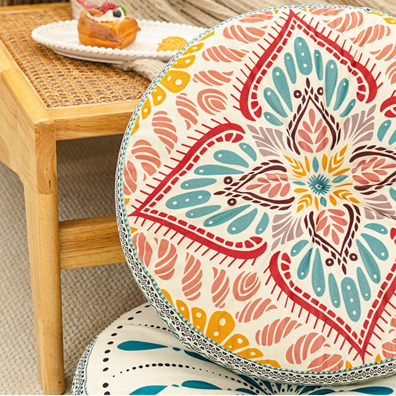 A close-up of a colorful bohemian round tatami cushion with intricate floral patterns on a wooden stool.