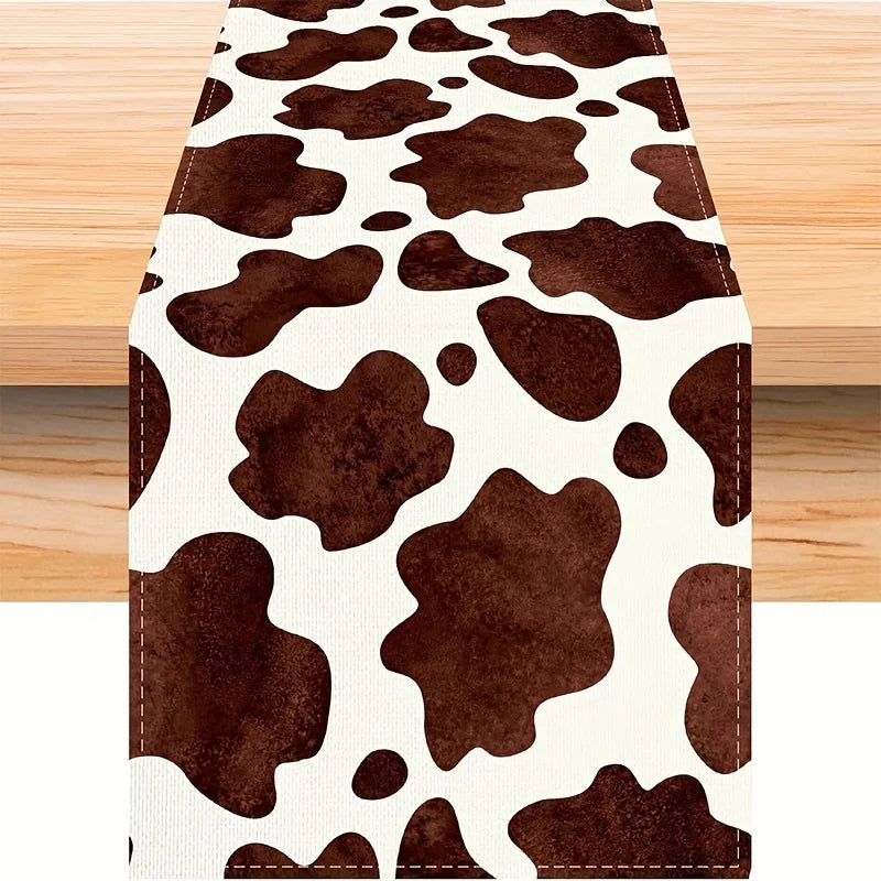 A brown and white cow print linen table runner displayed on a wooden surface.