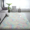 A fluffy tie-dye silk wool rug in pastel colors lies on a light gray floor next to a sofa and a window.
