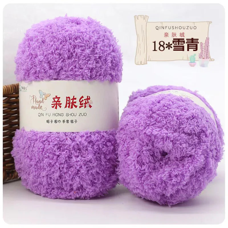 A purple ball of soft coral velvet yarn is shown next to its packaging and a wooden stick.
