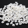 A pile of small, white imitation pearl flower spacer beads for DIY jewelry.