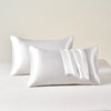 A set of two white satin pillowcases lying on a white surface.