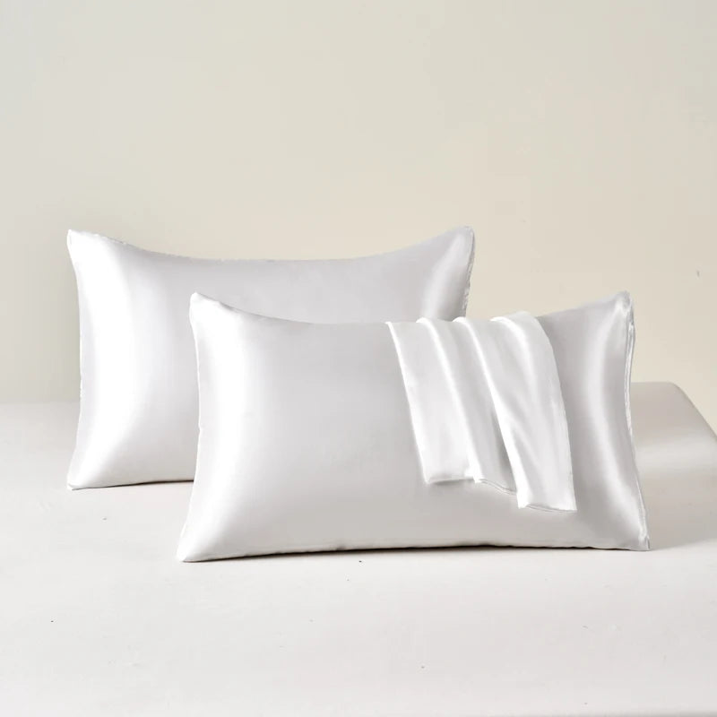 A set of two white satin pillowcases lying on a white surface.