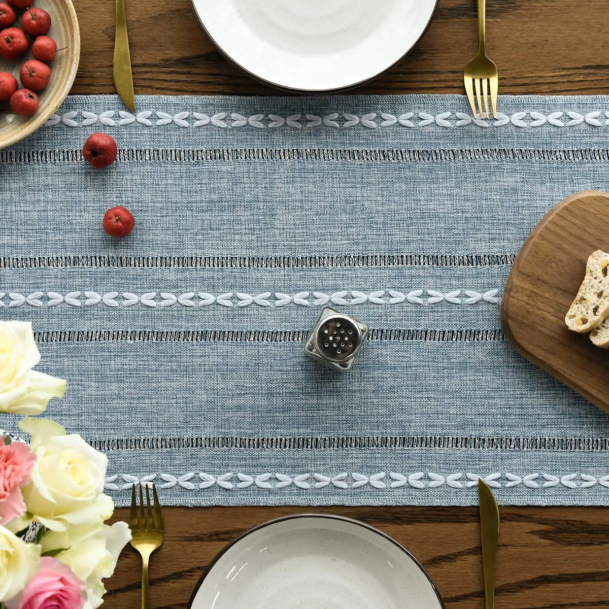A blue embroidered cotton linen table runner with white tassels laid on a wooden table.
