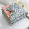 A light blue floral quilt with pink lining is displayed on a white surface.