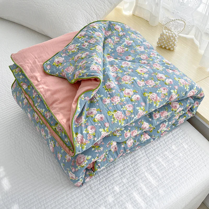 A light blue floral quilt with pink lining is displayed on a white surface.