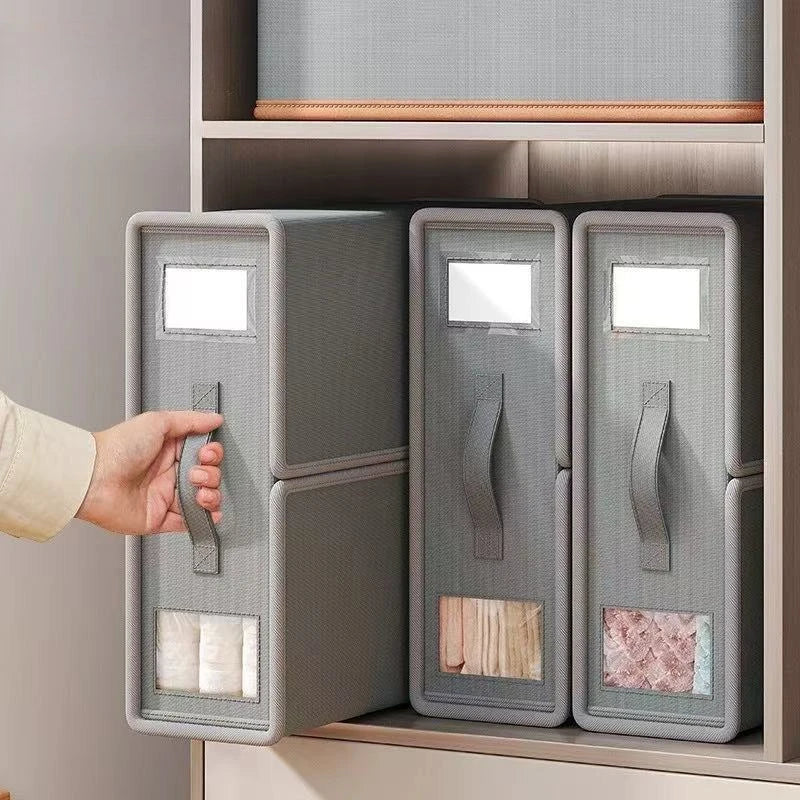 A hand opens a gray non-woven fabric storage box designed for bedding and clothing.