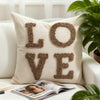 A beige knit pillow cover with the word LOVE embroidered in brown yarn rests on a white sofa.