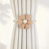 A pair of beige magnetic floral curtain tiebacks are shown against a white pleated curtain.