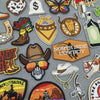A collection of embroidered iron-on patches featuring various western and cowboy motifs like skulls, bats, boots, and emblems