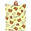 A woman is holding a yellow cartoon plush throw blanket featuring cute brown animal characters and the word Rilakkuma.