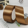 Roll of satin craft ribbon in a golden brown color shown on a white surface.