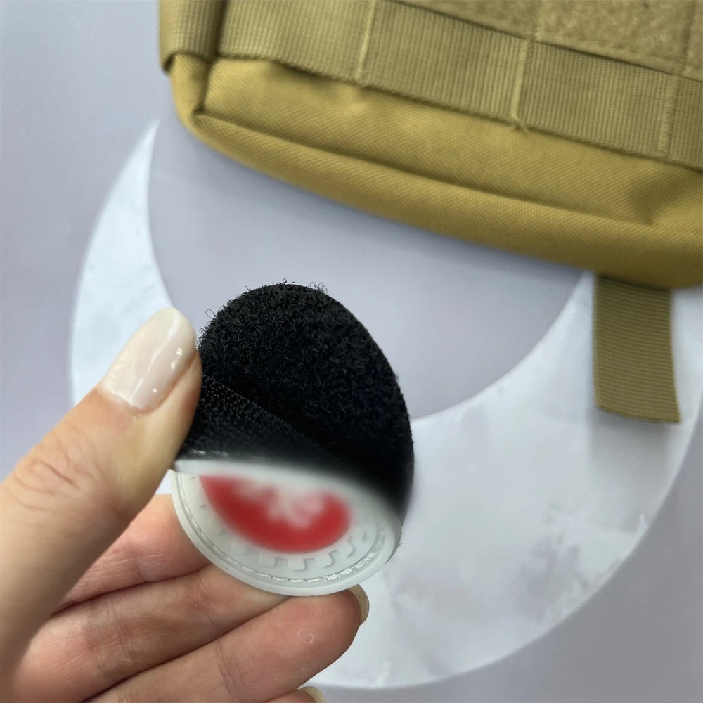A hand holds a black felt patch with a red circular design against a light background.