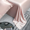 Pink luxury bamboo flat sheets draped on a table with a gold spoon and a silver measuring tool.
