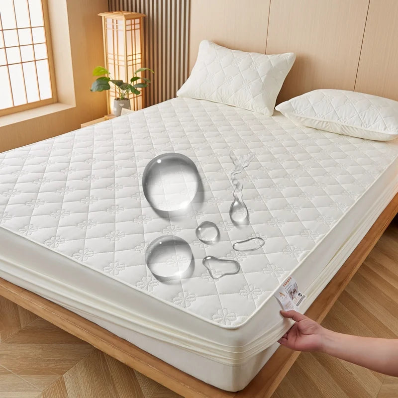 A white waterproof mattress protector is shown on a wooden bed frame, with various silicone molds resting on the surface.