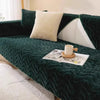 A dark emerald green plush sofa seat cushion cover with cream accent pillows and a magazine on the fabric.