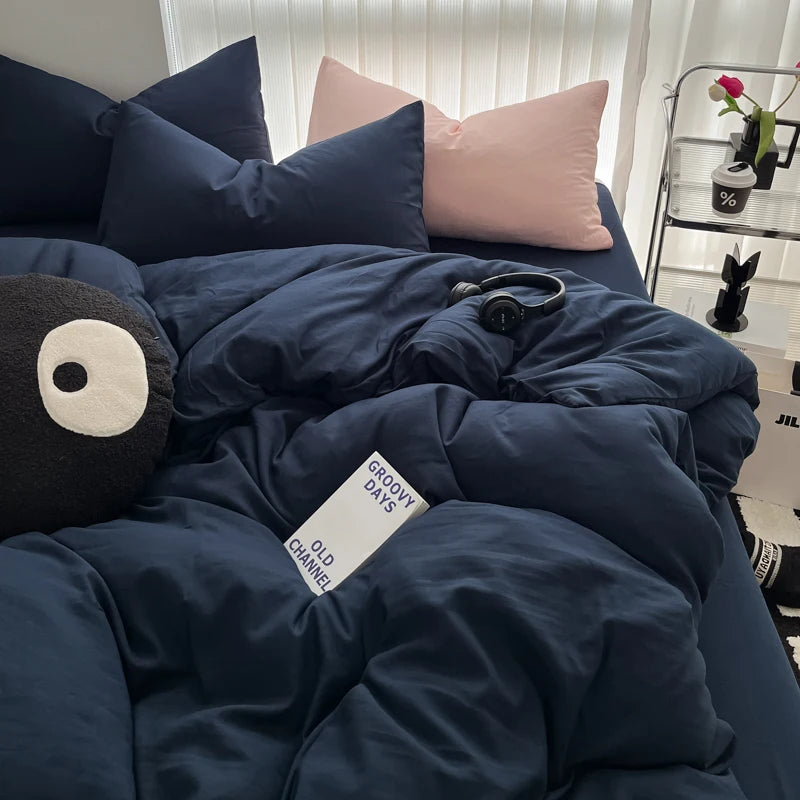 A dark blue duvet cover set with matching pillows and a black headphone resting on the bedding.